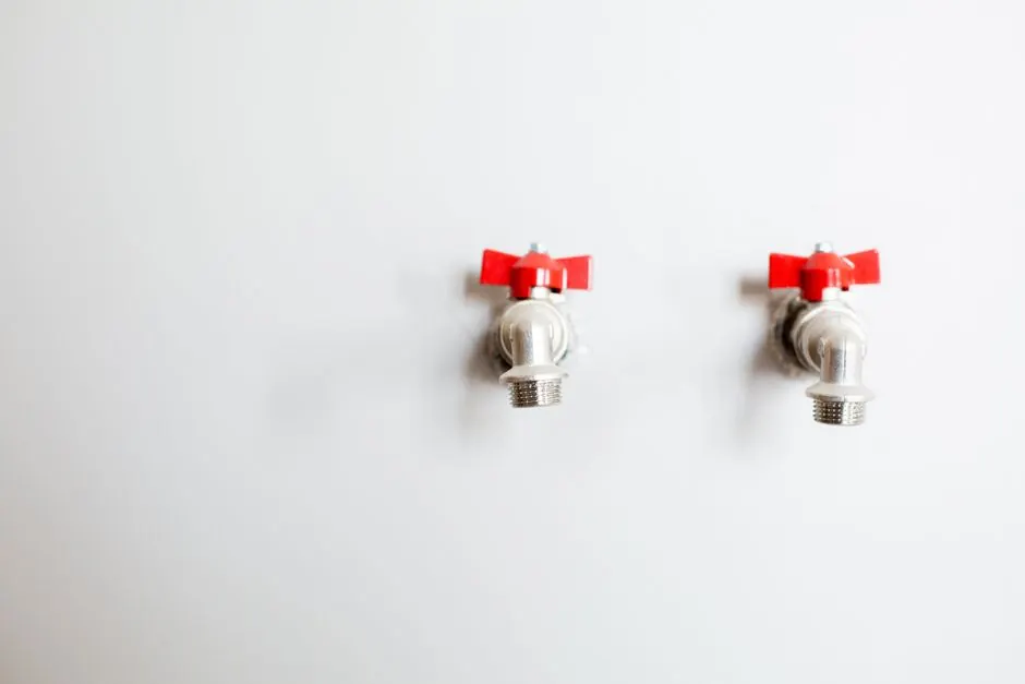 Close-up of two metal faucets with red handles against a white wall, showcasing plumbing detail.